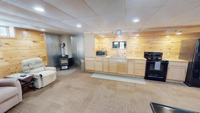 kitchen featuring sink, wooden walls, black appliances, a drop ceiling, and a wood stove