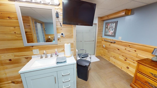 bathroom with a drop ceiling, vanity, and wood walls