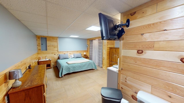 bedroom featuring a drop ceiling and wooden walls