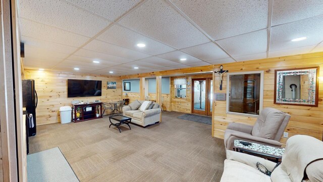 living room featuring wooden walls, carpet floors, and a drop ceiling