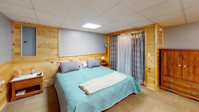 bedroom with a drop ceiling, electric panel, and wood walls