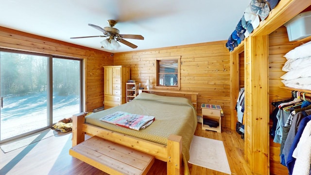 bedroom with ceiling fan, wood-type flooring, wood walls, and access to outside