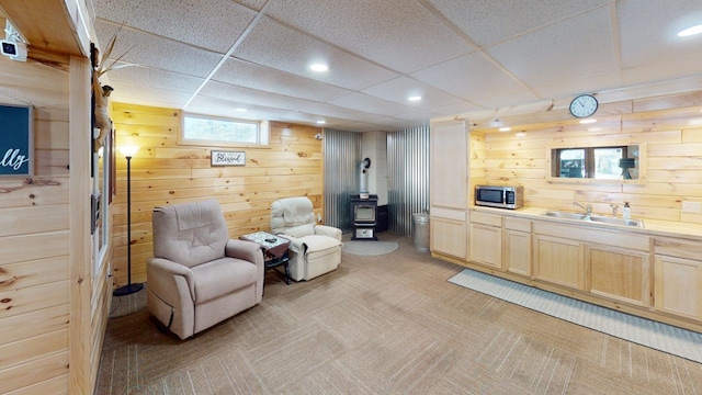 sitting room with a paneled ceiling, sink, a wood stove, and wood walls