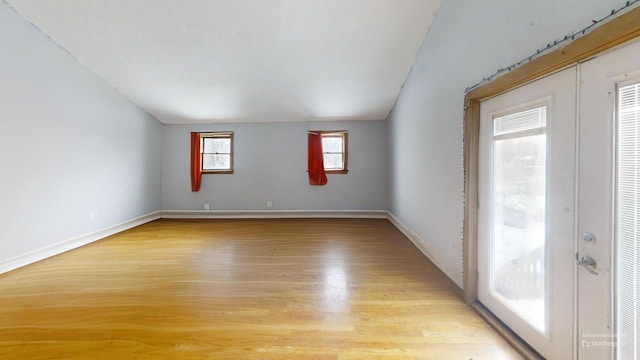 spare room with vaulted ceiling, light wood-type flooring, and french doors