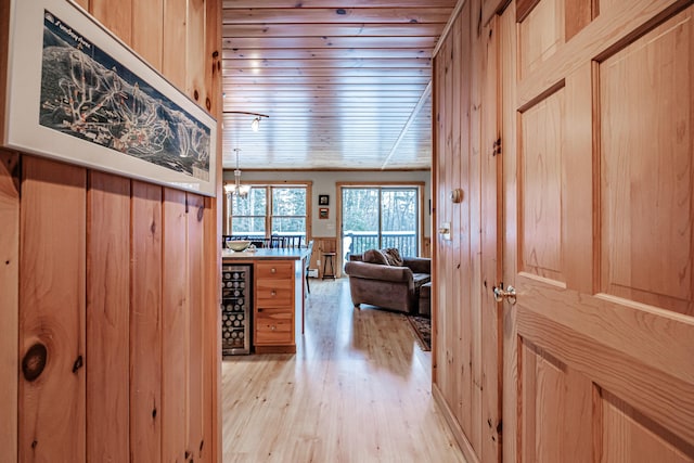 corridor featuring light hardwood / wood-style flooring, a notable chandelier, and wood walls