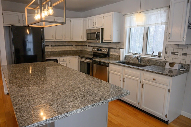 kitchen with sink, white cabinets, dark stone counters, hanging light fixtures, and stainless steel appliances