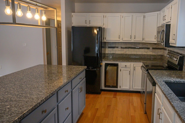 kitchen with appliances with stainless steel finishes, white cabinetry, dark stone counters, hanging light fixtures, and light hardwood / wood-style flooring