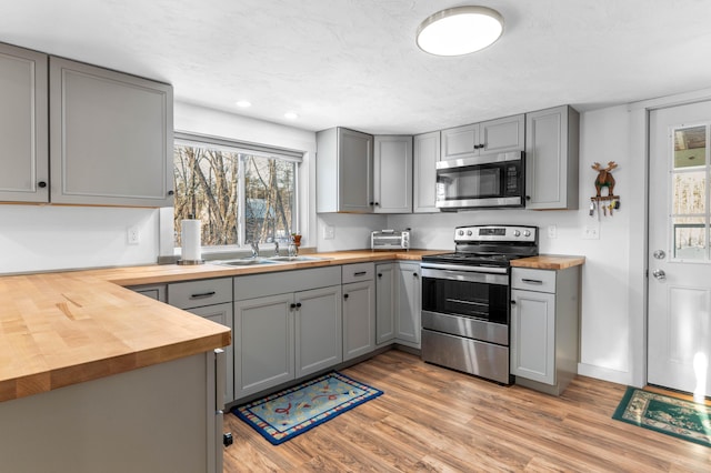 kitchen featuring sink, gray cabinetry, wooden counters, light hardwood / wood-style flooring, and appliances with stainless steel finishes