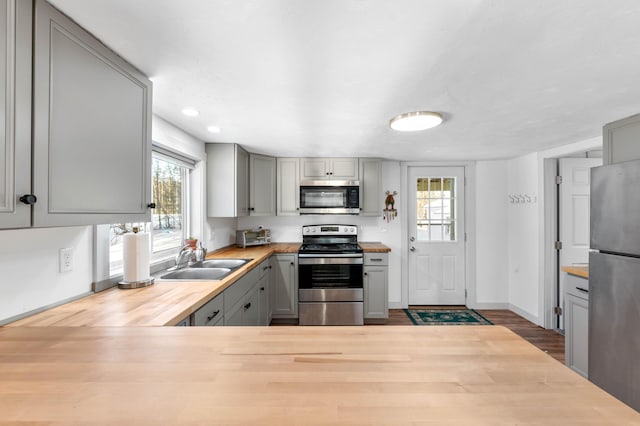 kitchen with gray cabinetry, butcher block countertops, sink, and appliances with stainless steel finishes