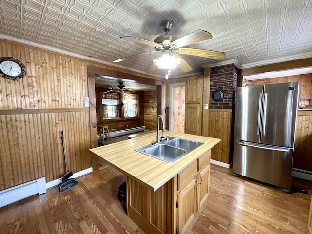 kitchen featuring sink, hardwood / wood-style flooring, stainless steel fridge, wooden walls, and an island with sink