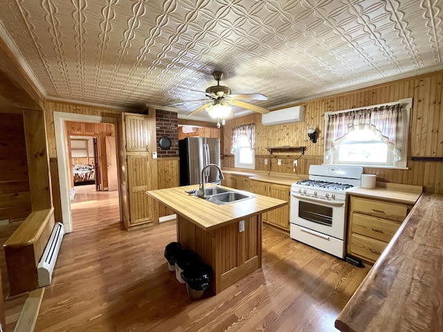 kitchen with sink, a wall mounted AC, stainless steel fridge, a baseboard heating unit, and gas range gas stove