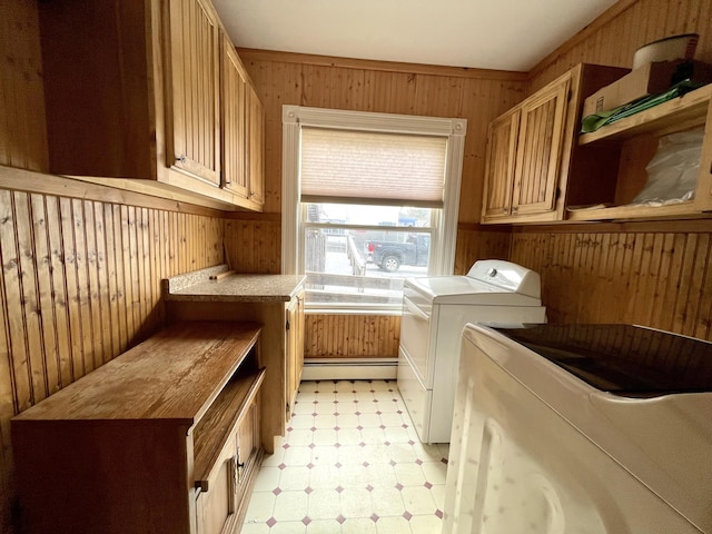 clothes washing area featuring cabinets, a baseboard radiator, wooden walls, and washer and clothes dryer