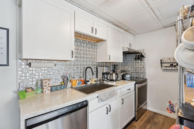 kitchen with appliances with stainless steel finishes, sink, white cabinets, dark hardwood / wood-style flooring, and light stone counters