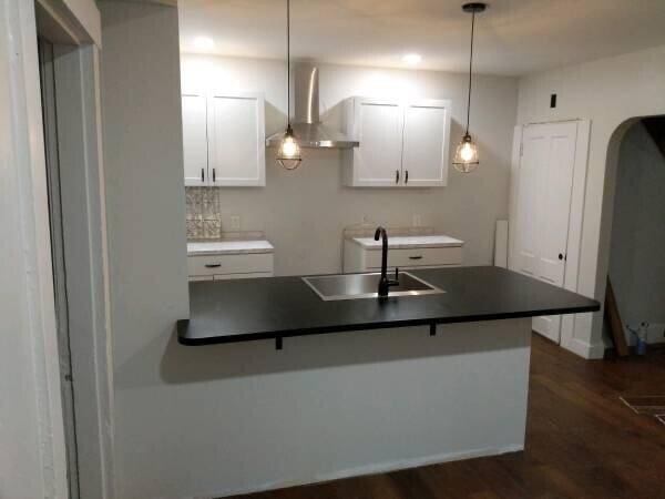 kitchen with a breakfast bar, dark hardwood / wood-style floors, sink, white cabinets, and hanging light fixtures