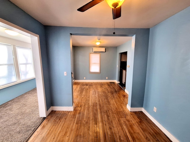 empty room with wood-type flooring, a wall mounted air conditioner, and ceiling fan