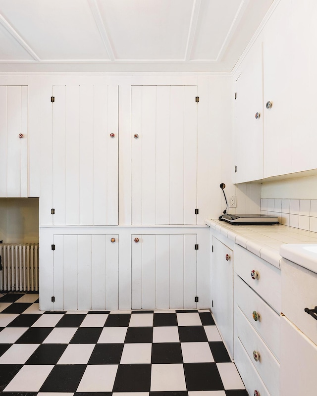 interior space with radiator heating unit, tile counters, and white cabinets