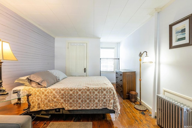 bedroom with crown molding, radiator heating unit, wooden walls, and hardwood / wood-style flooring