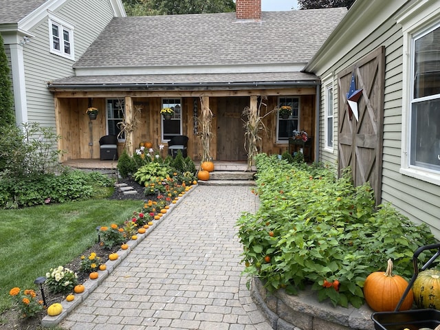 property entrance with roof with shingles, a yard, and a chimney