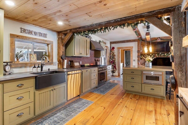 kitchen with light wood finished floors, stainless steel appliances, a sink, green cabinetry, and wall chimney exhaust hood