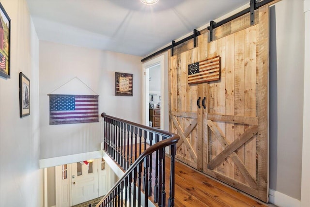 hall featuring a barn door, wood finished floors, an upstairs landing, and baseboards