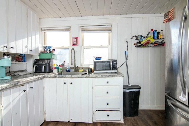 kitchen featuring appliances with stainless steel finishes, sink, white cabinets, and wood walls