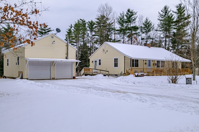 snow covered rear of property featuring a garage and covered porch