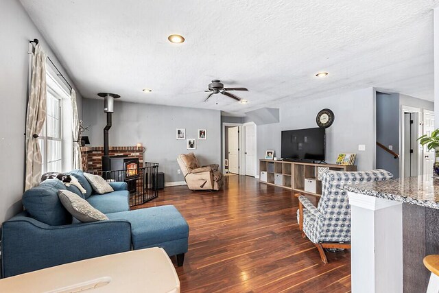 living room featuring ceiling fan, a wood stove, a textured ceiling, and dark hardwood / wood-style flooring