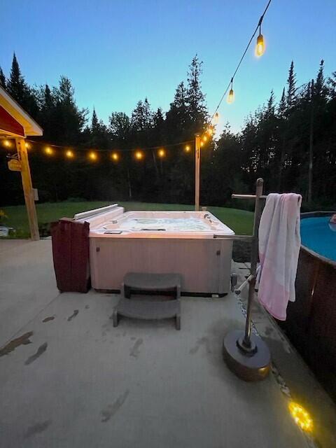 pool at dusk with a hot tub and a patio