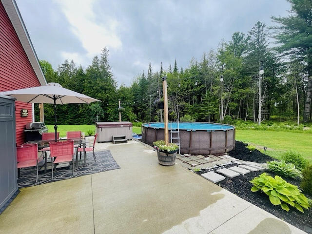 view of patio / terrace with a swimming pool with hot tub and a grill