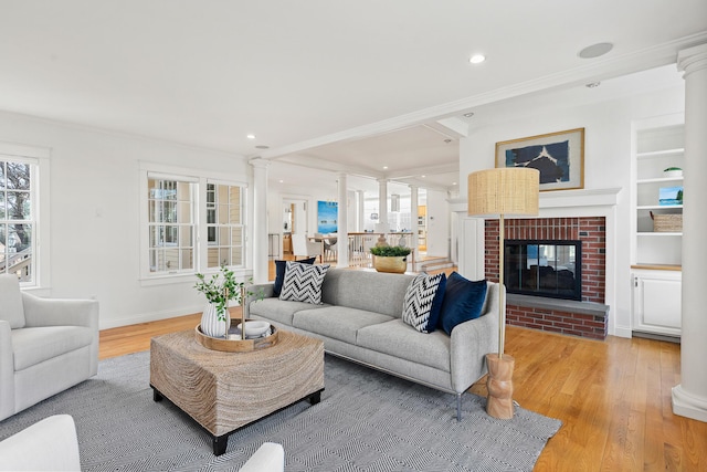 living room featuring wood finished floors, ornamental molding, ornate columns, and a healthy amount of sunlight
