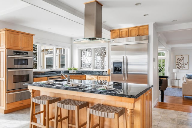 kitchen featuring crown molding, a warming drawer, island exhaust hood, a center island with sink, and appliances with stainless steel finishes