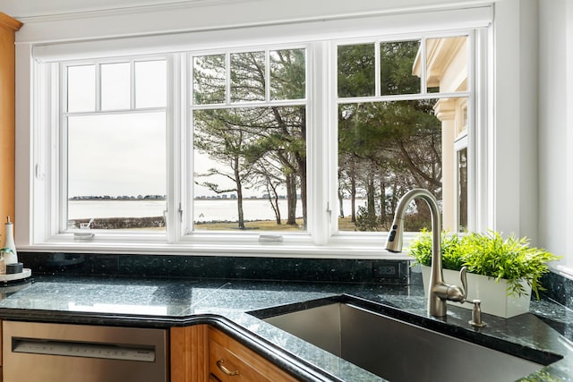 interior details featuring brown cabinets, dishwasher, dark stone countertops, and a sink