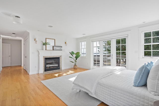 bedroom with light wood-type flooring, a tiled fireplace, baseboards, and access to outside