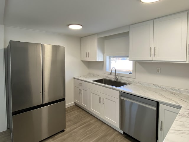 kitchen with sink, white cabinets, light hardwood / wood-style floors, stainless steel appliances, and light stone countertops