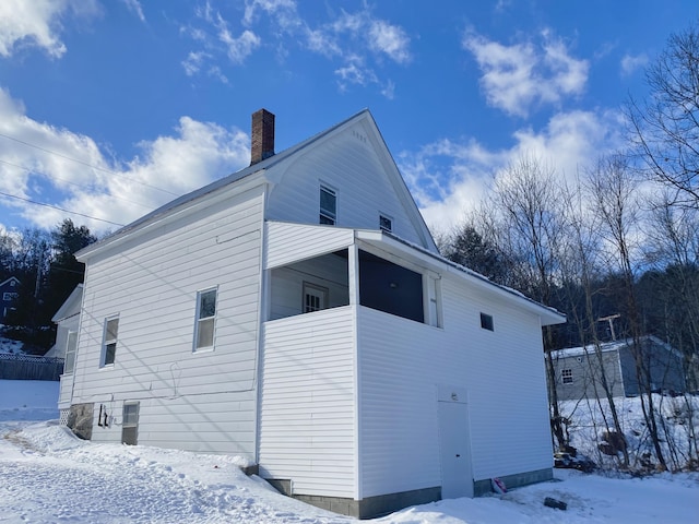 snow covered back of property featuring a balcony