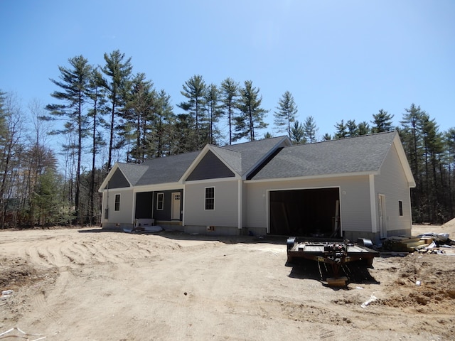 unfinished property featuring a shingled roof, dirt driveway, and a garage