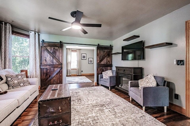 living room featuring dark wood-type flooring, ceiling fan, and a barn door