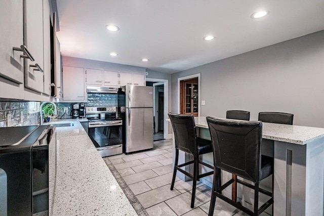 kitchen featuring sink, stainless steel appliances, a kitchen breakfast bar, tasteful backsplash, and light stone counters