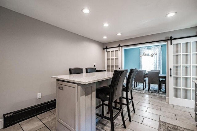 kitchen featuring light tile patterned floors, a breakfast bar, light stone countertops, a kitchen island, and a barn door