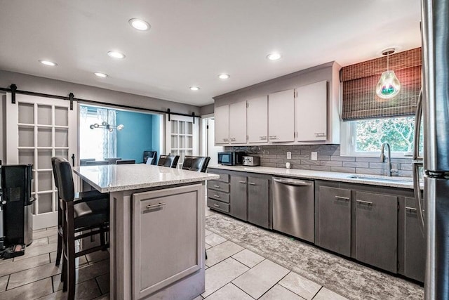 kitchen featuring a kitchen bar, a center island, hanging light fixtures, appliances with stainless steel finishes, and a barn door