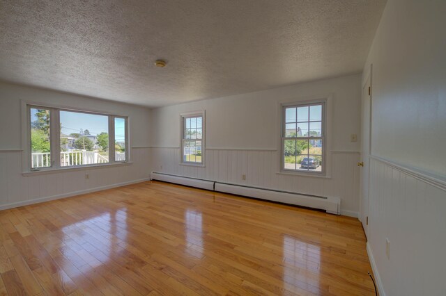 3 Sea Breeze Ave, Biddeford, ME 04005 - unfurnished room featuring baseboard heating, a textured ceiling, light wood-style flooring, wainscoting, and healthy amount of natural light
