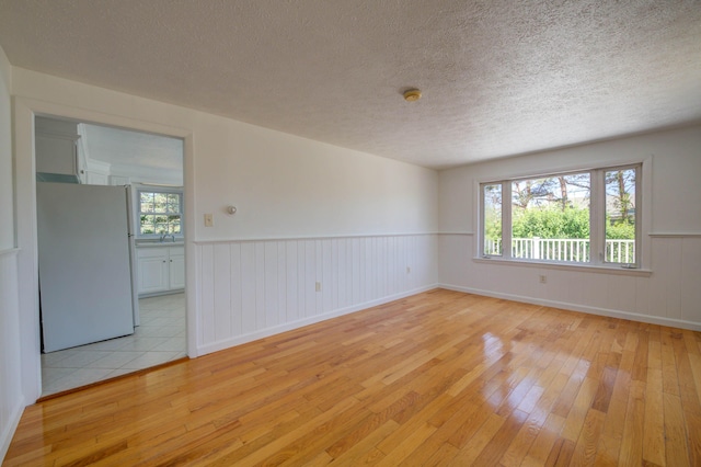 3 Sea Breeze Ave, Biddeford, ME 04005 - spare room with light wood-style flooring, a textured ceiling, a wainscoted wall, healthy amount of natural light, and a smoke detector