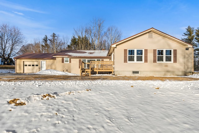 snow covered rear of property with a wooden deck and a garage