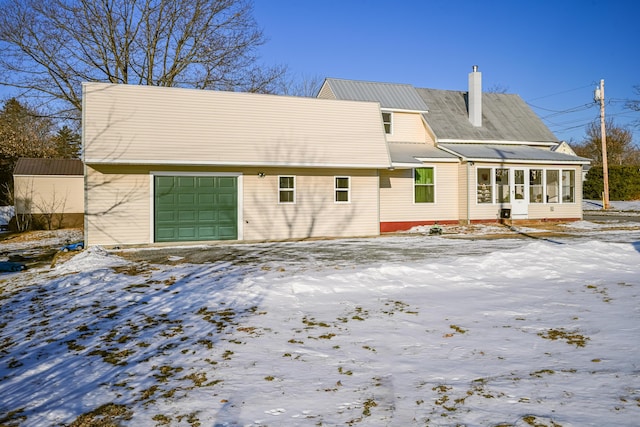 snow covered rear of property featuring a garage and a sunroom