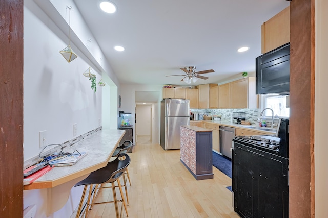 kitchen with sink, appliances with stainless steel finishes, backsplash, a kitchen breakfast bar, and light brown cabinets