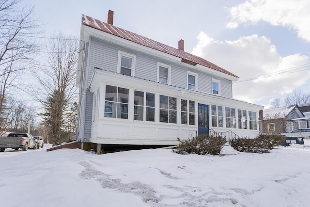 snow covered house featuring a sunroom