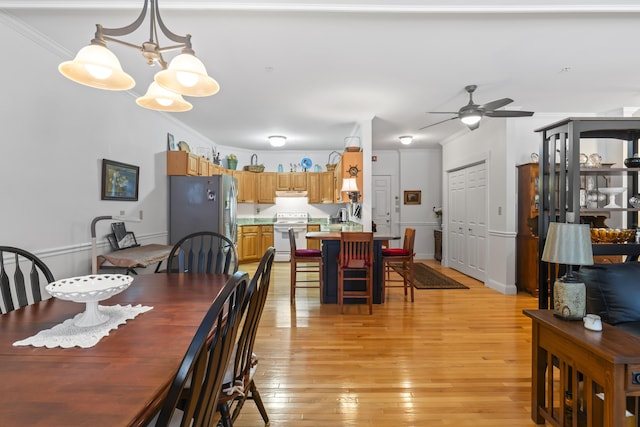 dining area with ornamental molding, sink, ceiling fan with notable chandelier, and light hardwood / wood-style flooring