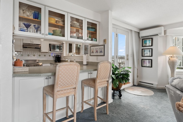 bar featuring an AC wall unit, under cabinet range hood, stainless steel appliances, carpet flooring, and a baseboard radiator