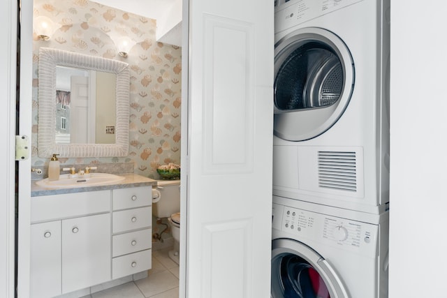 clothes washing area featuring a sink, wallpapered walls, light tile patterned flooring, stacked washer / dryer, and laundry area