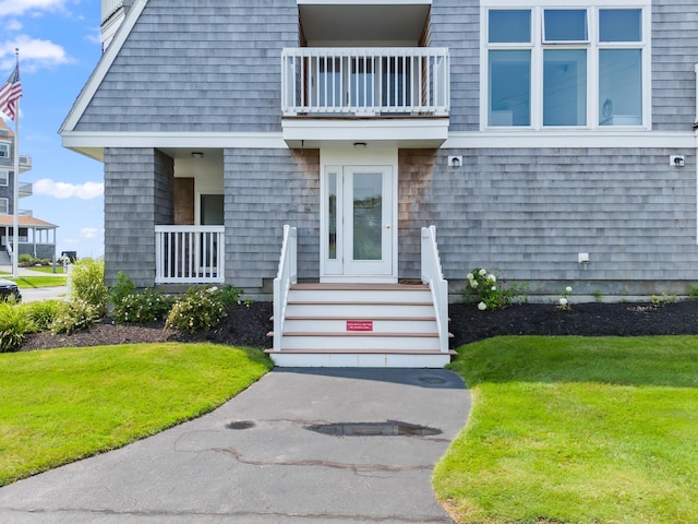 view of exterior entry with a yard and a balcony